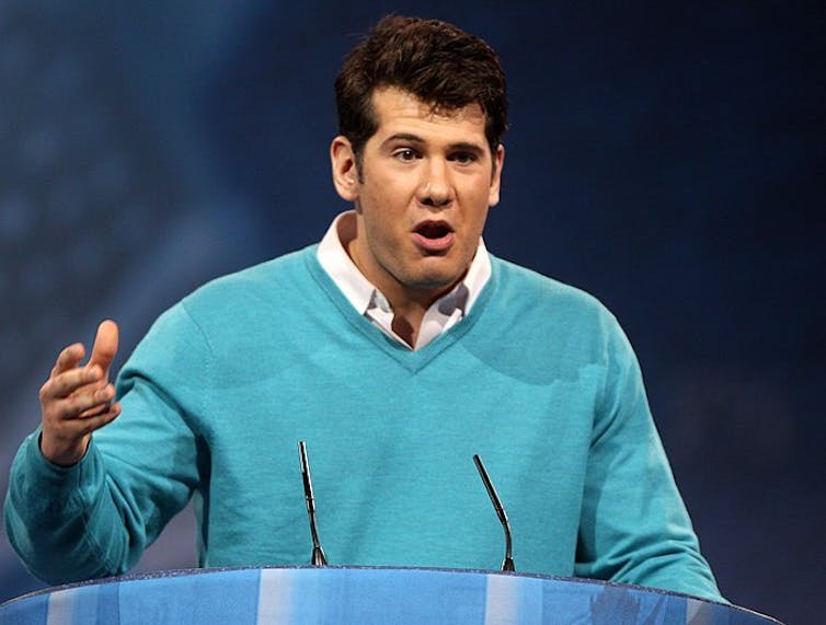 Man in blue sweater speaking at a podium.
