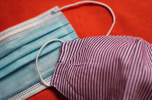 A surgical mask and a cloth mask on a red background.