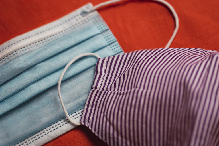 A surgical mask and a cloth mask on a red background.