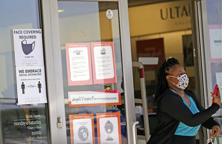 Una mujer sale de una tienda en cuya puerta hay un cartel con normas sobre el uso de la mascarilla.