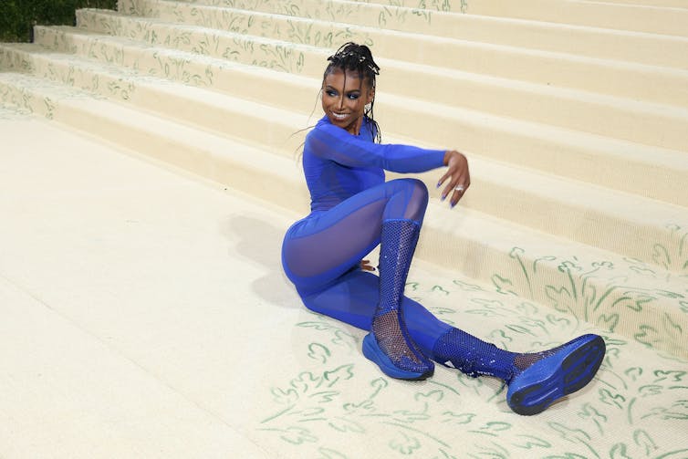 Gymnast Nia Dennis dressed all in blue poses for photo at bottom of stairway