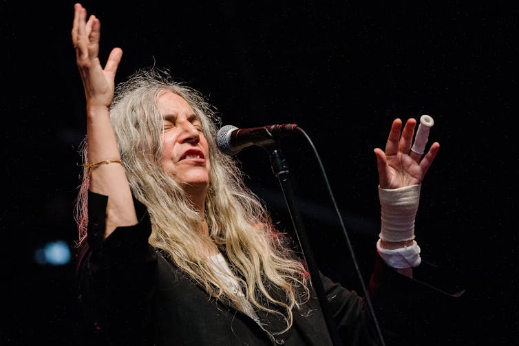 Patti Smith performing behind a microphone with long grey hair