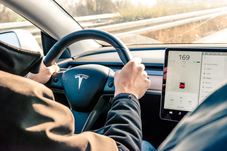 Interior of a car, driver's hands on the steering wheel, a computer display mounted on the dashboard