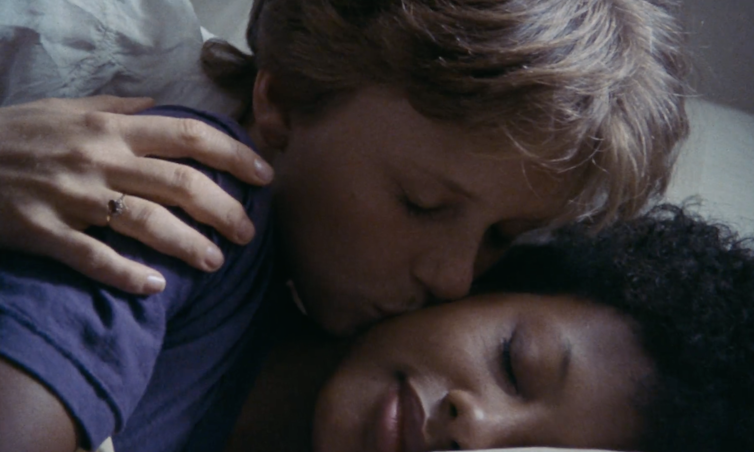A lesbian couple, one white woman and one Black woman, embrace in bed