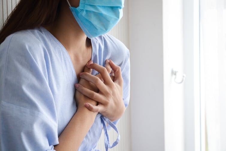 Woman in a mask holds her chest above her heart.