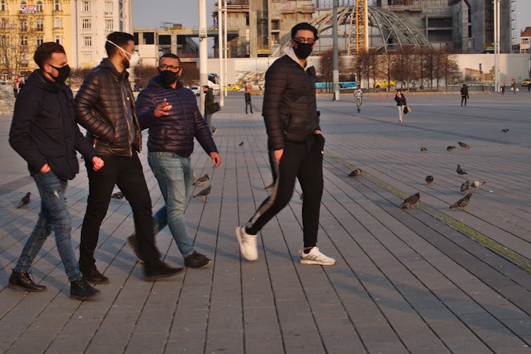 Four Turkish men walk across an open town space.