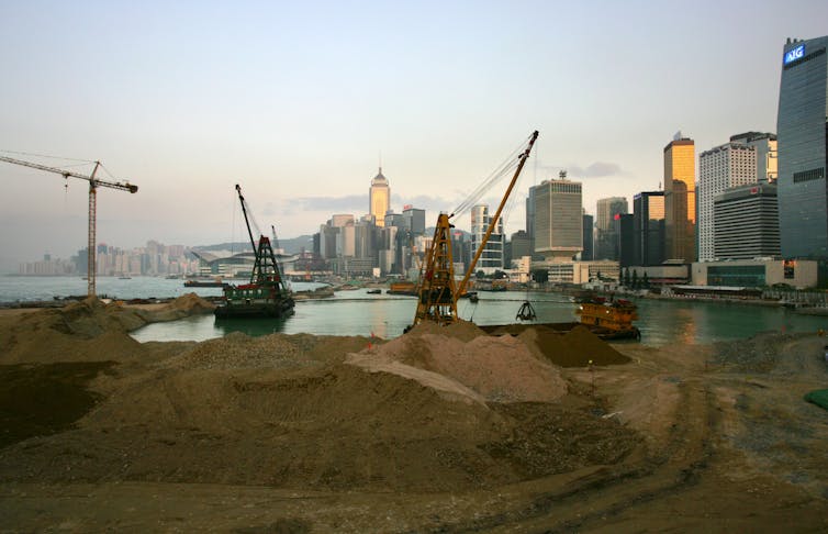 Diggers and cranes move sand against the bay, skyscrapers in background
