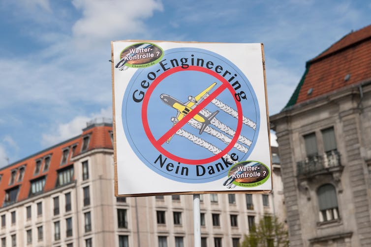 A placard of a stop sign superposed over a picture of a plane trailing white smoke reads 'Geo-engineering: Nein Danke'