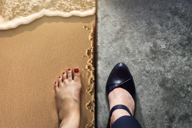 One foot on a beach and another in a high-heeled shoe