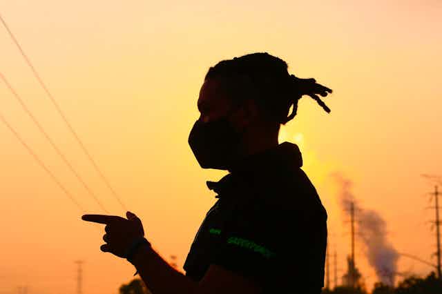 A man wears a face mask with a power plant in the background.