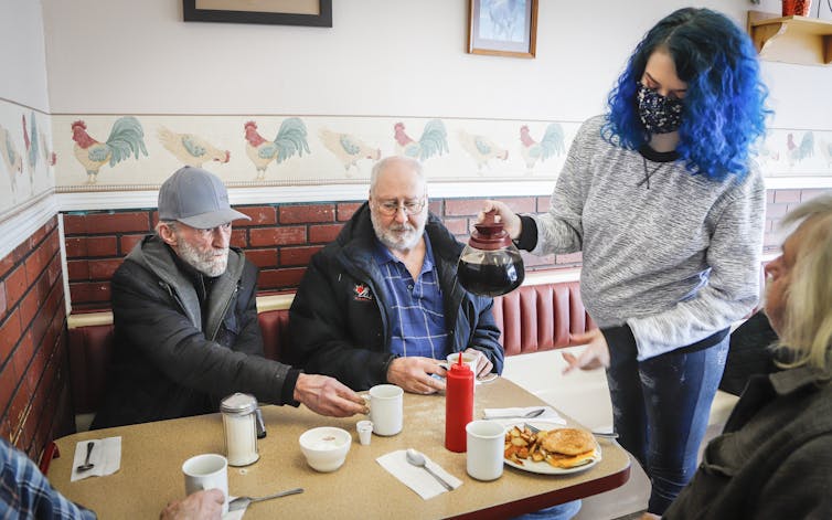 A waitress wearing a mask serves patrons.