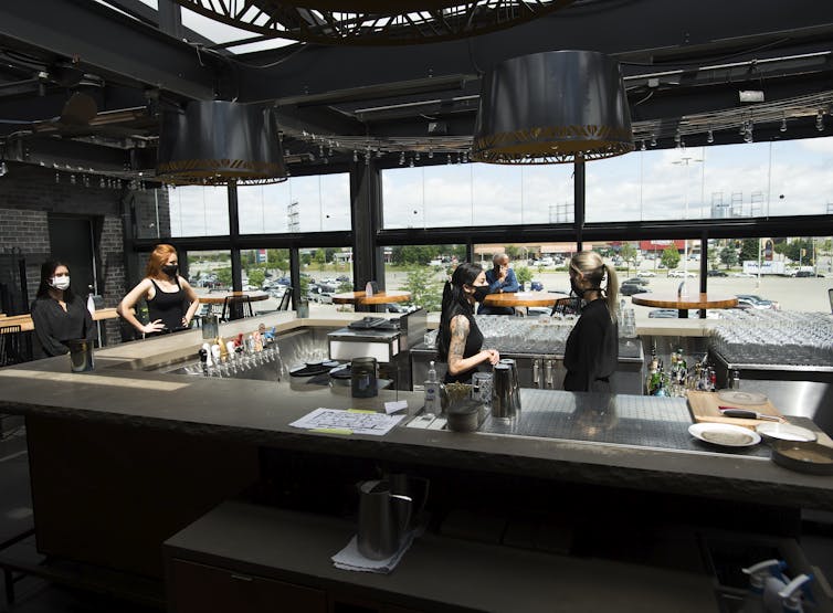 Bartenders and wait staff, all wearing masks, inside a restaurant.