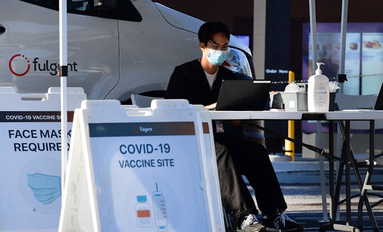 vaccine clinic worker seated at table near signs