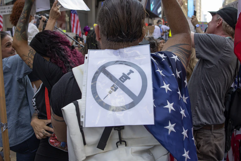 man at a rally with an anti-vaccine sign on his back