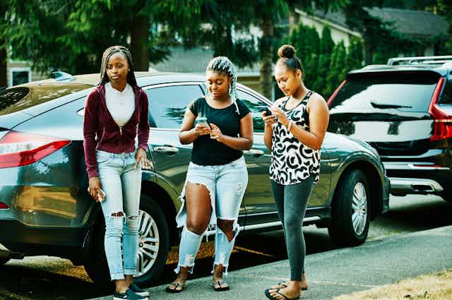Tres chicas adolescentes en una acera mirando sus teléfonos celulares