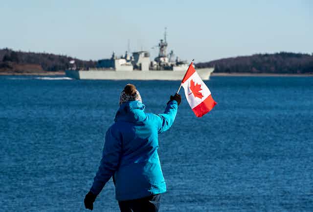 A woman waves a Canadian flag as she watches a frigate leave Halifax harbour.