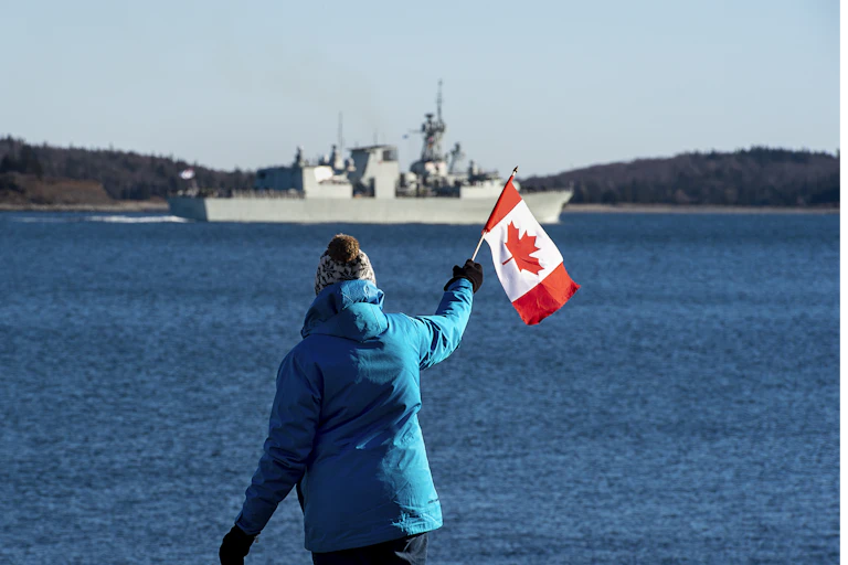 A woman waves a Canadian flag as she watches a frigate leave Halifax harbour.