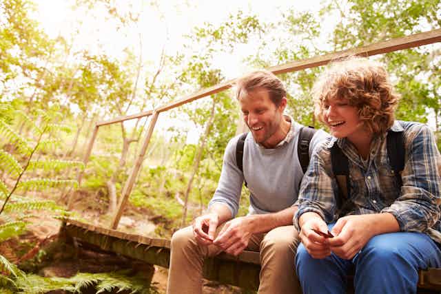 Father and son sitting on bridge and chatting.