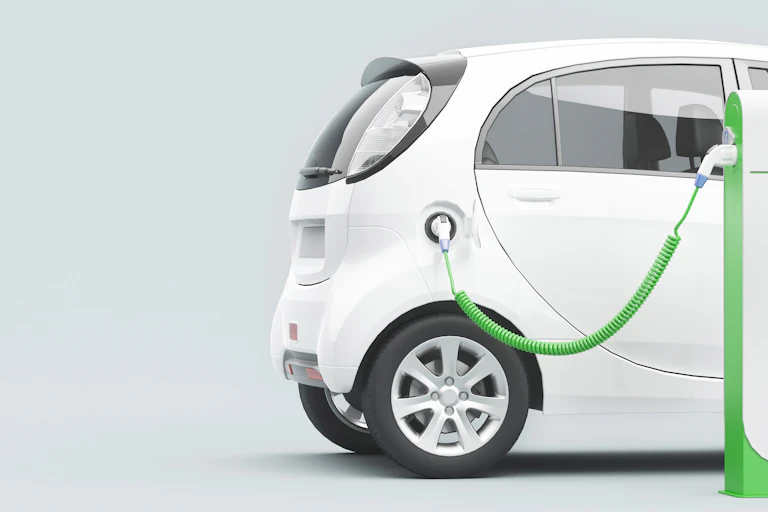 A white compact car connected to a green charging point.