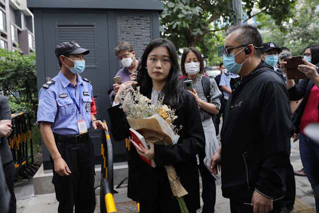 A Chinese woman carrying a bunch of flowers walks past police offers and officials wearing masks outside a court in Haidian, China.