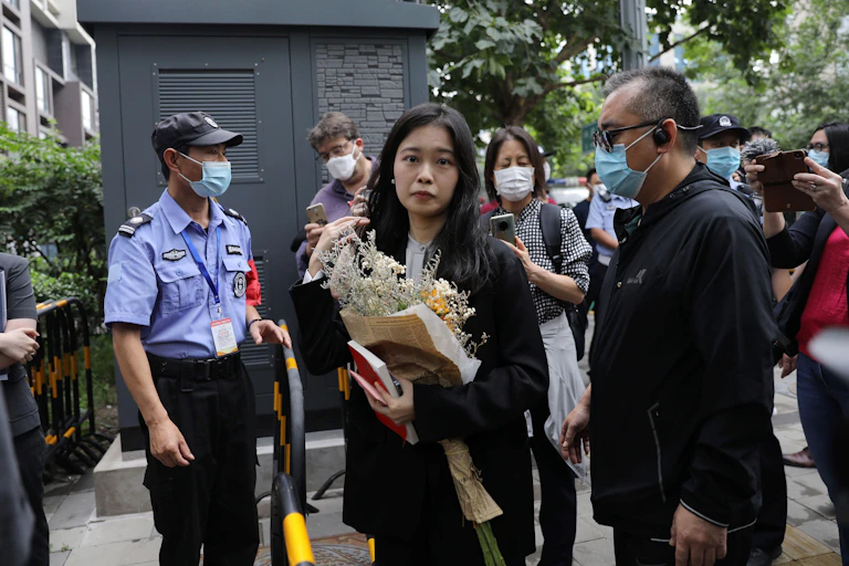 A Chinese woman carrying a bunch of flowers walks past police offers and officials wearing masks outside a court in Haidian, China.