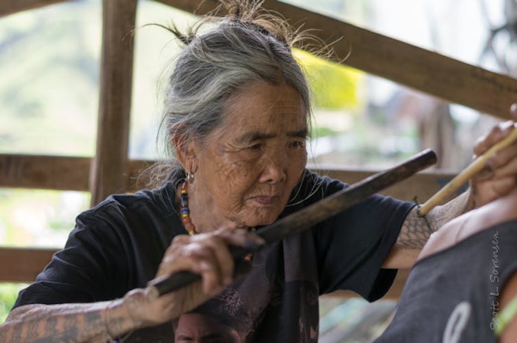 A woman making a traditional mambabatok tattoo using a mallet and needles in the Philippines.