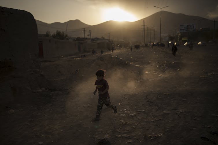 An Afghan boy plays beside a road as the sun sets.