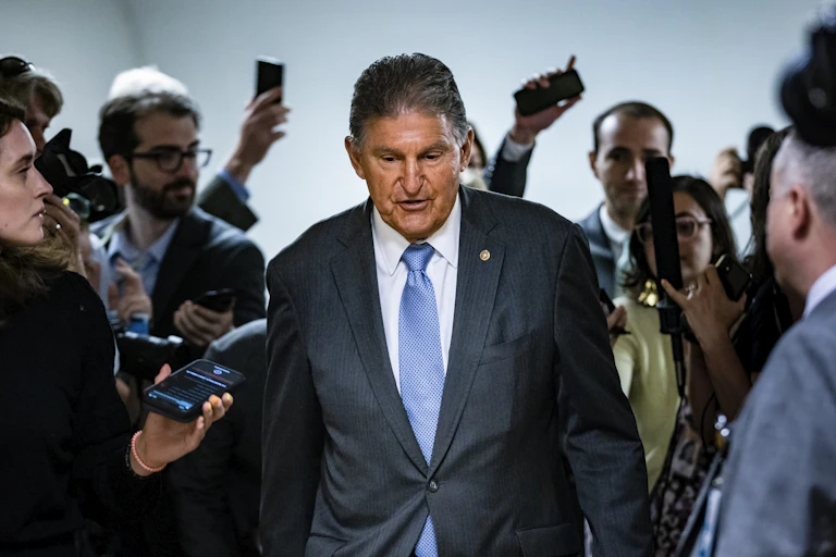 Joe Manchin talking reporters as he walks down a hall