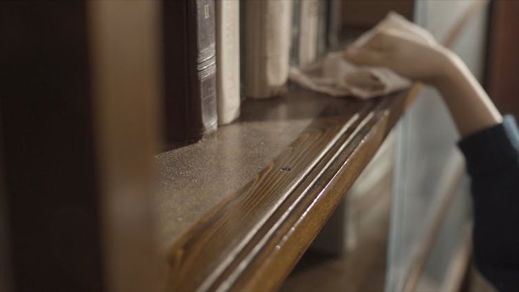 A person wipes dust from a shelf.