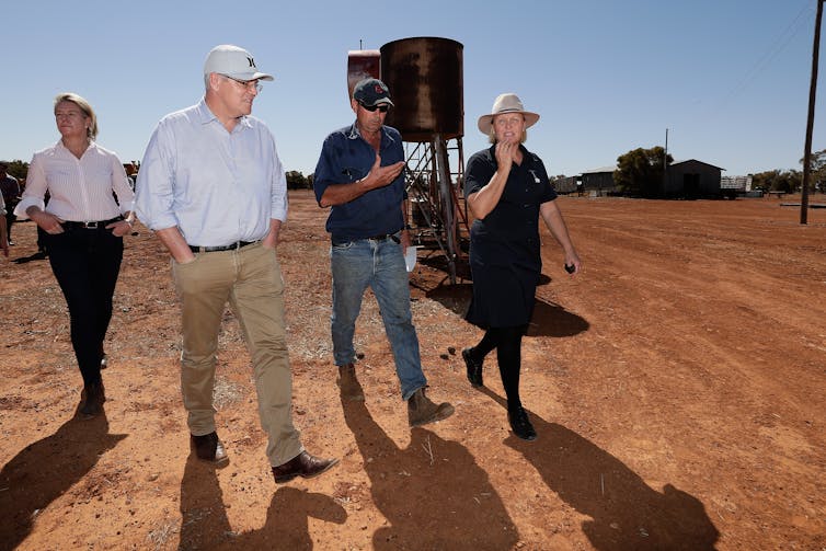 four people walk through dusty farm