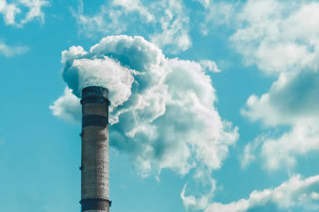 An industrial chimney spewing white smoke in a blue sky.