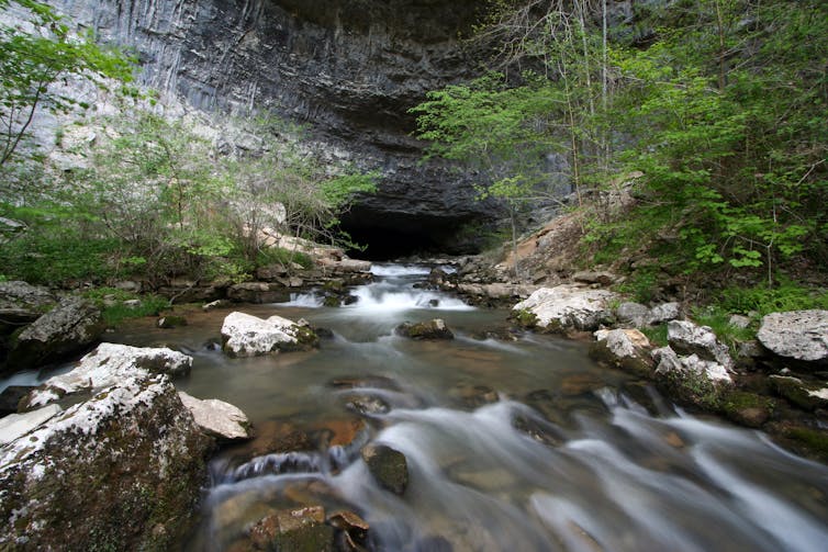 small cave opening with rushing stream in foreground