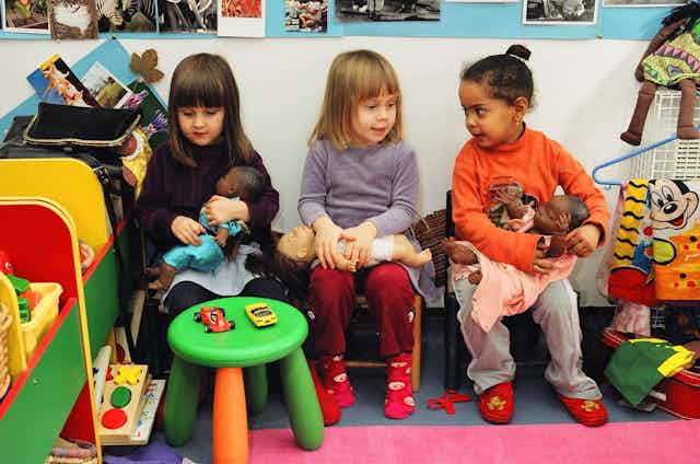 Three little girls play with dolls in a nursery room