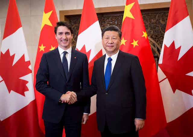 Justin Trudeau serre la main de  Xi Jinping devant des drapeaux canadiens et chinois