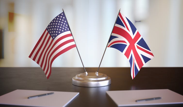 US and UK flags on a desk next to paper and pens.