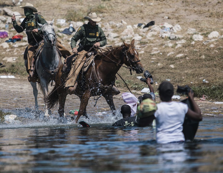 U.S. Customs and Border Protection agents on horseback draw whips as they encounter Haitian migrants partially submerged in water.
