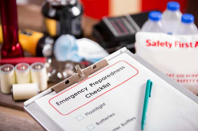  An emergency prep list with items in the background including flashlight, radio, batteries, water