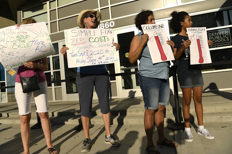 Four people hold signs protesting high temperatures in school classrooms