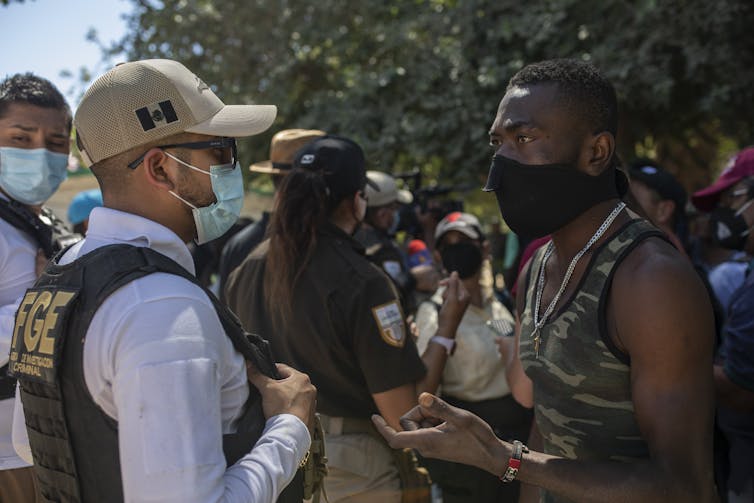 A uniformed Mexican police officer talks with a Haitian migrant wearing a mask.