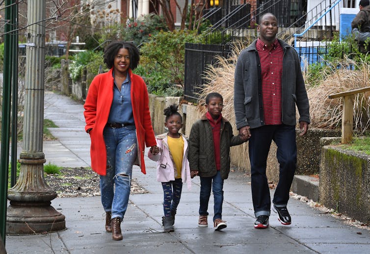 Mother, father and two small children hold hands while walking down street