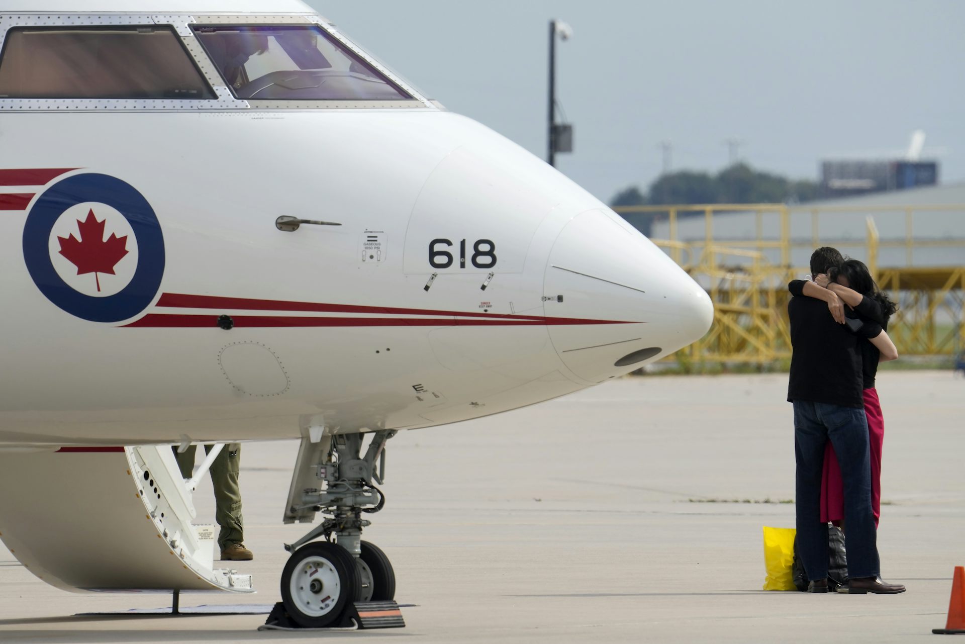 A man and woman embrace in front of a plane.