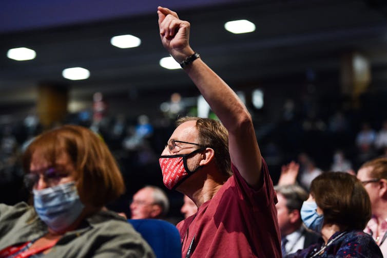 A man wearing a Labour branded face covering holds his hand in the air to vote at party conference.