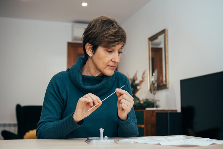 Middle-aged woman with short hair sits at a desk examining the instructions of a home rapid antigen test.