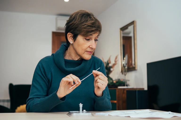 Middle-aged woman with short hair sits at a desk examining the instructions of a home rapid antigen test.