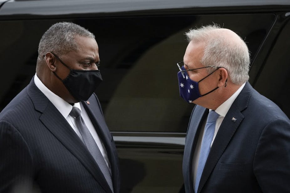 Le secrétaire de la défense américain, Lloyd Austin et le premier ministre australien, Scott Morrison se font face en costume devant une voiture noire.