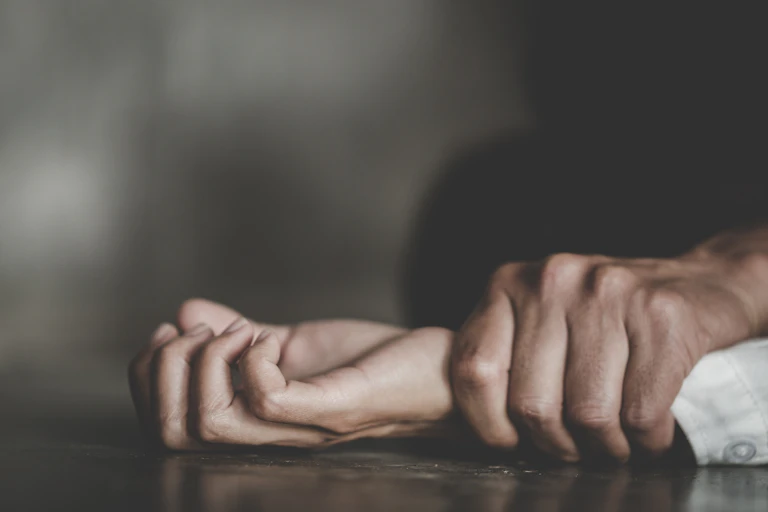 A close-up of a man's hand holding a woman's wrist and pinning her to the floor