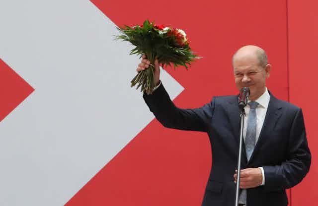 Olaf Scholz holding up a bouquet of flowers after winning the German election.