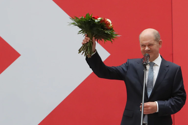 Olaf Scholz holding up a bouquet of flowers after winning the German election.