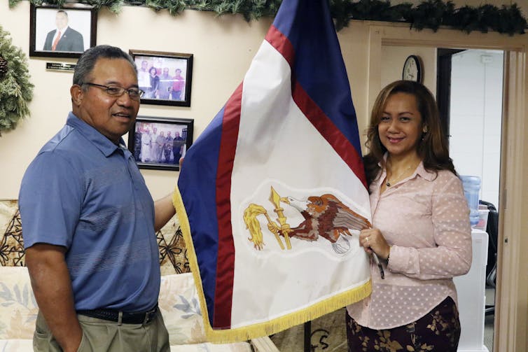 Two people stand next to a flag