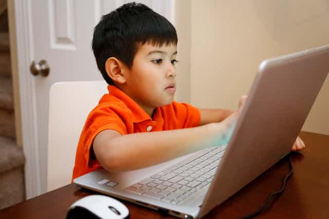 A Native American youngster is at home doing schoolwork on his laptop.